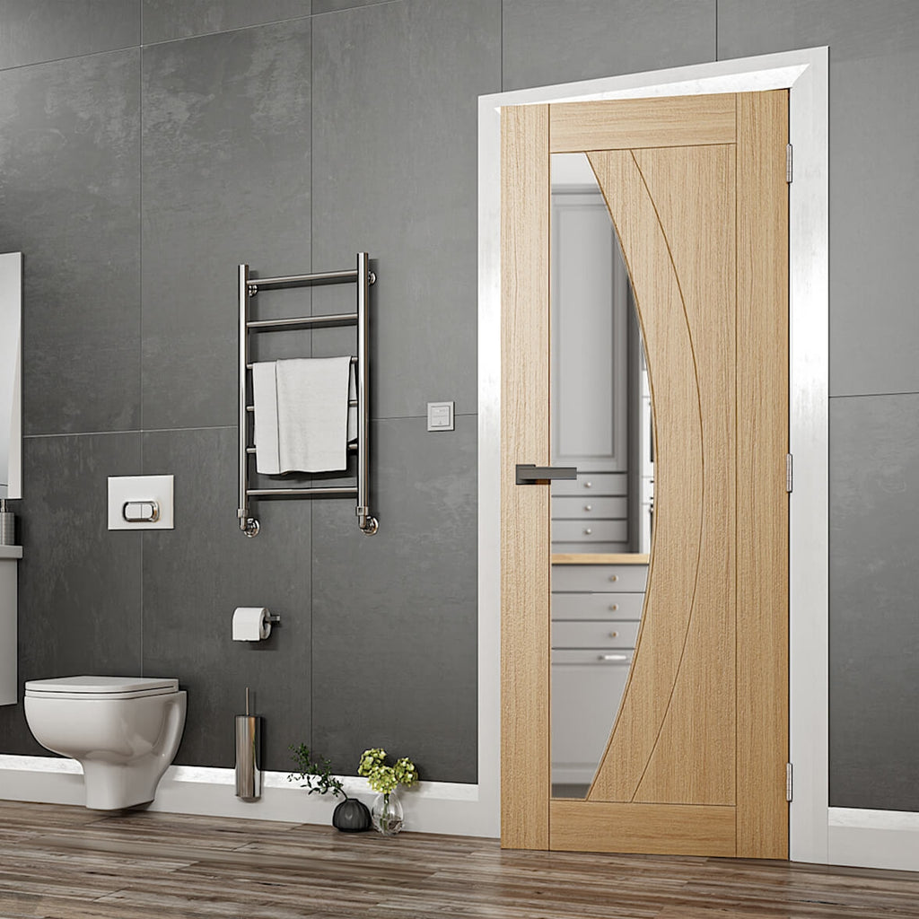 Ravello Oak Clear Glazed Internal Door - The Ravello door has an offset clear glazed panel with a detailed groove which follows the arch of the glazing, the frame and skirting and all in white, there is a bathroom suite to the left of the images and a small chrome radiator halfway up the wall, flooring is in laminate with a dark wood colour effect.