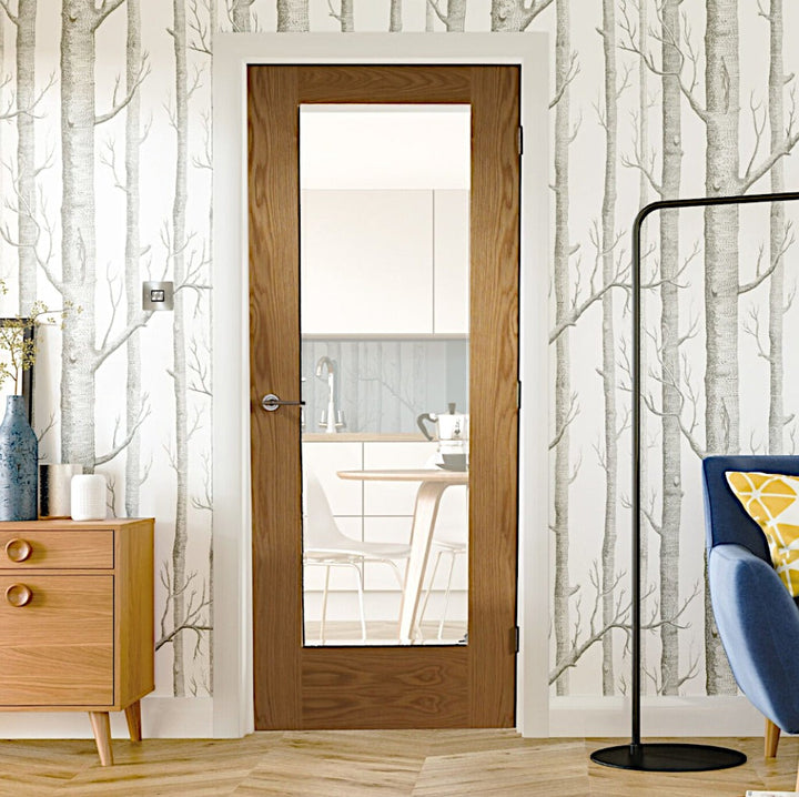Pattern 10 Oak Clear Glazed Fire Door - The pattern 10 door style has a large clear glazed panel in the centre an is fitted with white architrave and skirting, a tree/branch effect wallpaper in monotone colours. An Oak sideboard is present to the right of the image with a blur corner of a sofa visible to the left