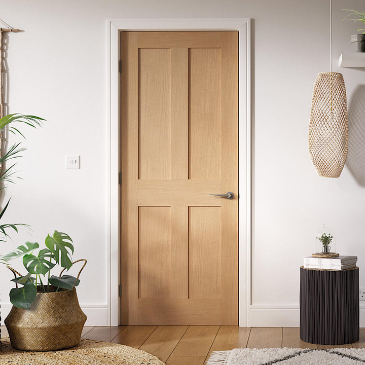 London Oak Internal Door Fully Finished - A contemporary oak style internal door with four flat panel, the door frame and architrave along with the walls are all white, the floor is in oak Oak with rattan pendant light and plants to the left of the image