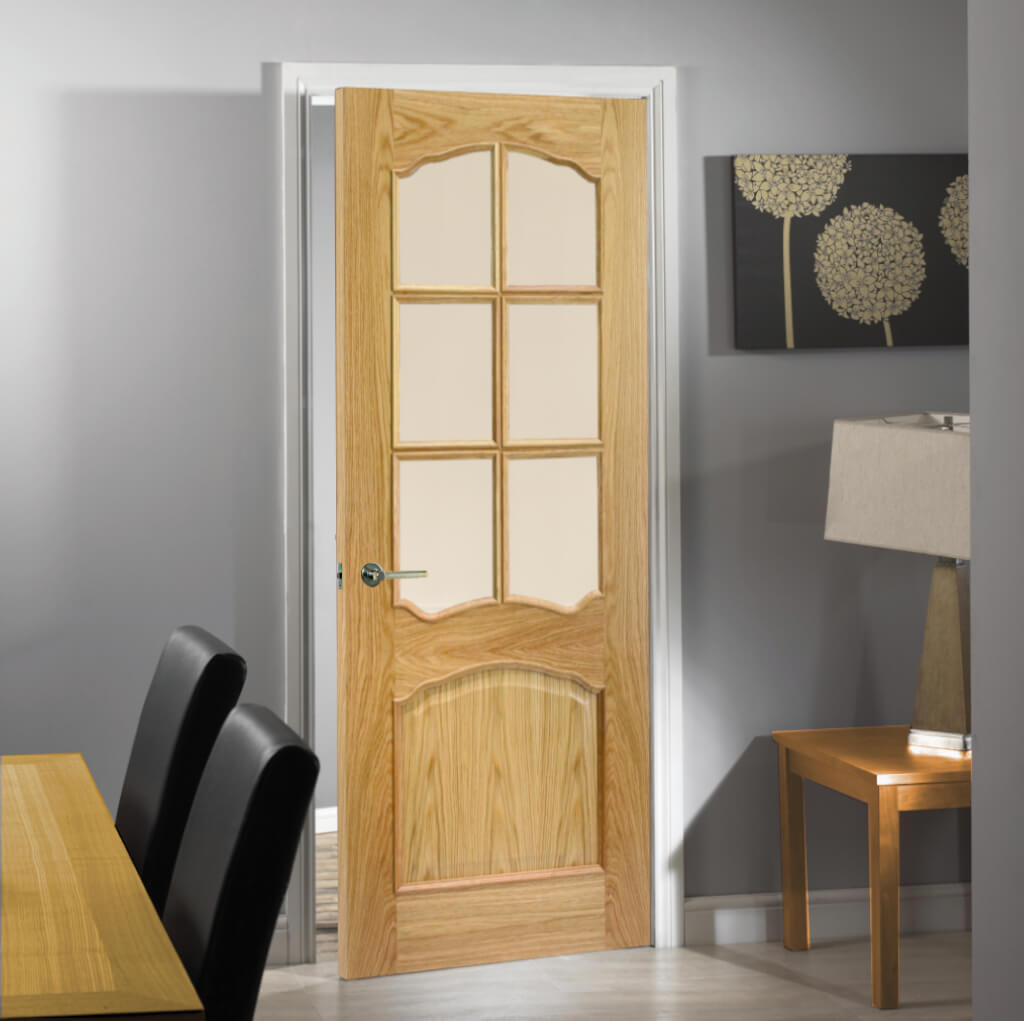 Oak Riviera Glazed Internal Door 6L RM2S - This particular door has six ornate panels of glazing with a decorative lower panel, wall and floor are in a shade of grey with and Oak lamp table to the right and an Oak dining table to the left of the image.